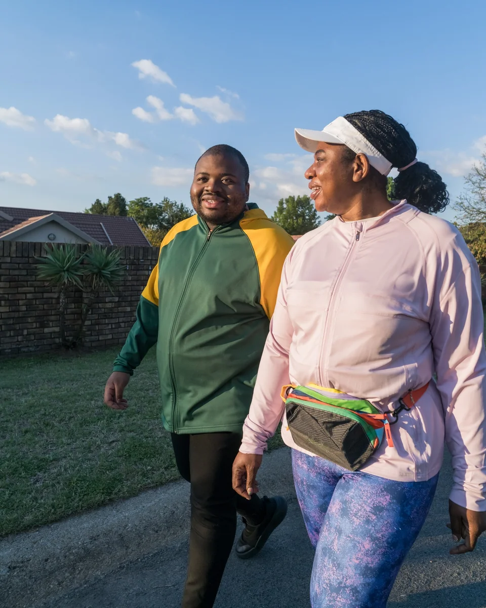 Madam O walking and talking with a fellow walker on a suburban road.